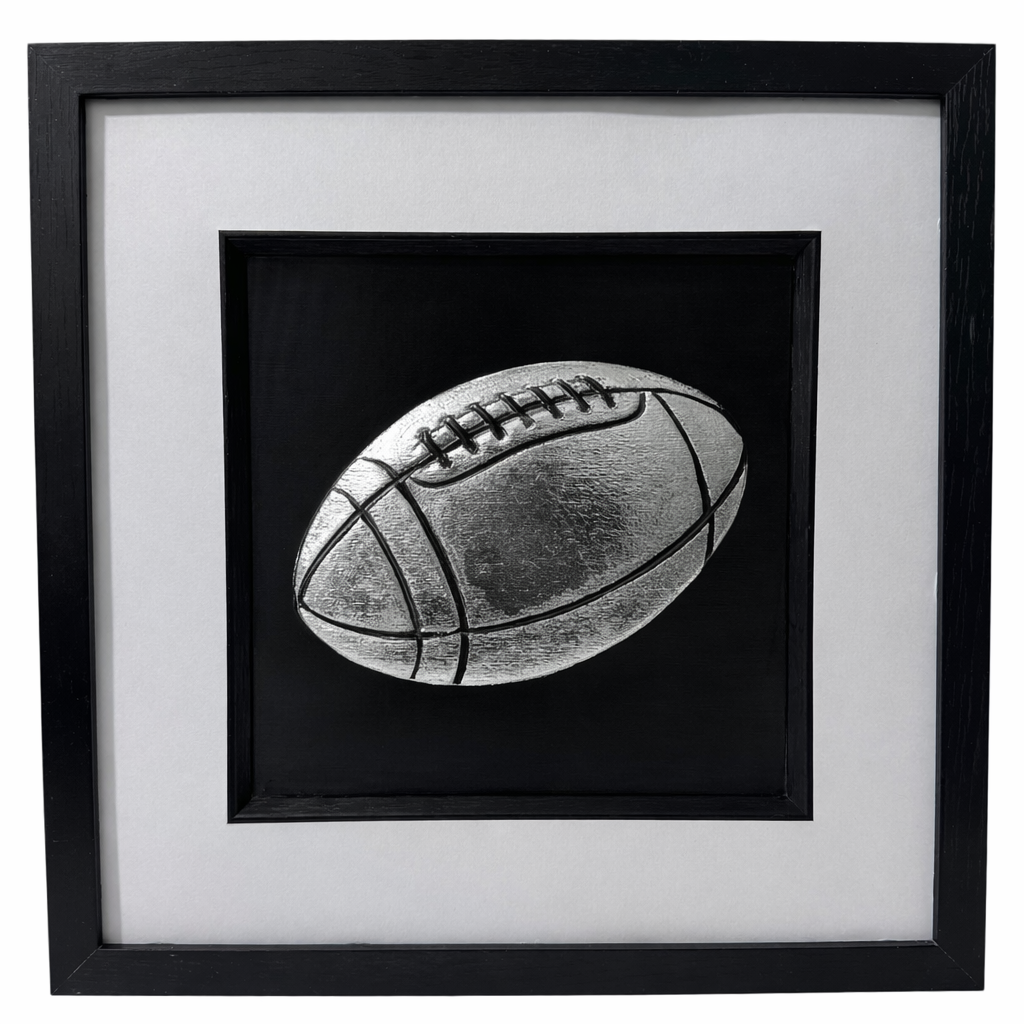 Front view of rugby ball relief artwork in Silver Leaf on black background in a black box frame with white mount