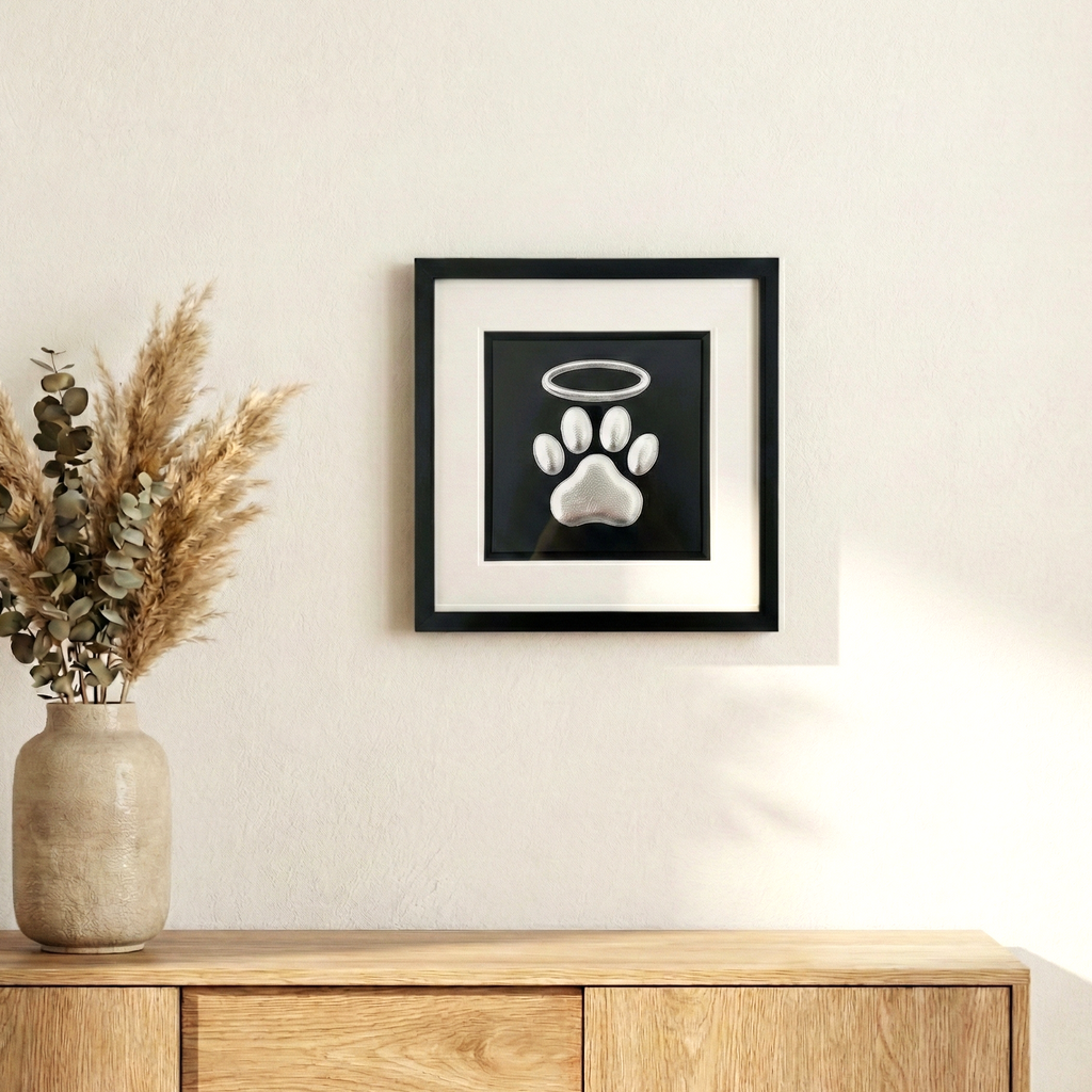 Framed dog paw print halo memorial wall art in silver leaf, styled on a neutral wall above a wooden sideboard with dried pampas in a vase.