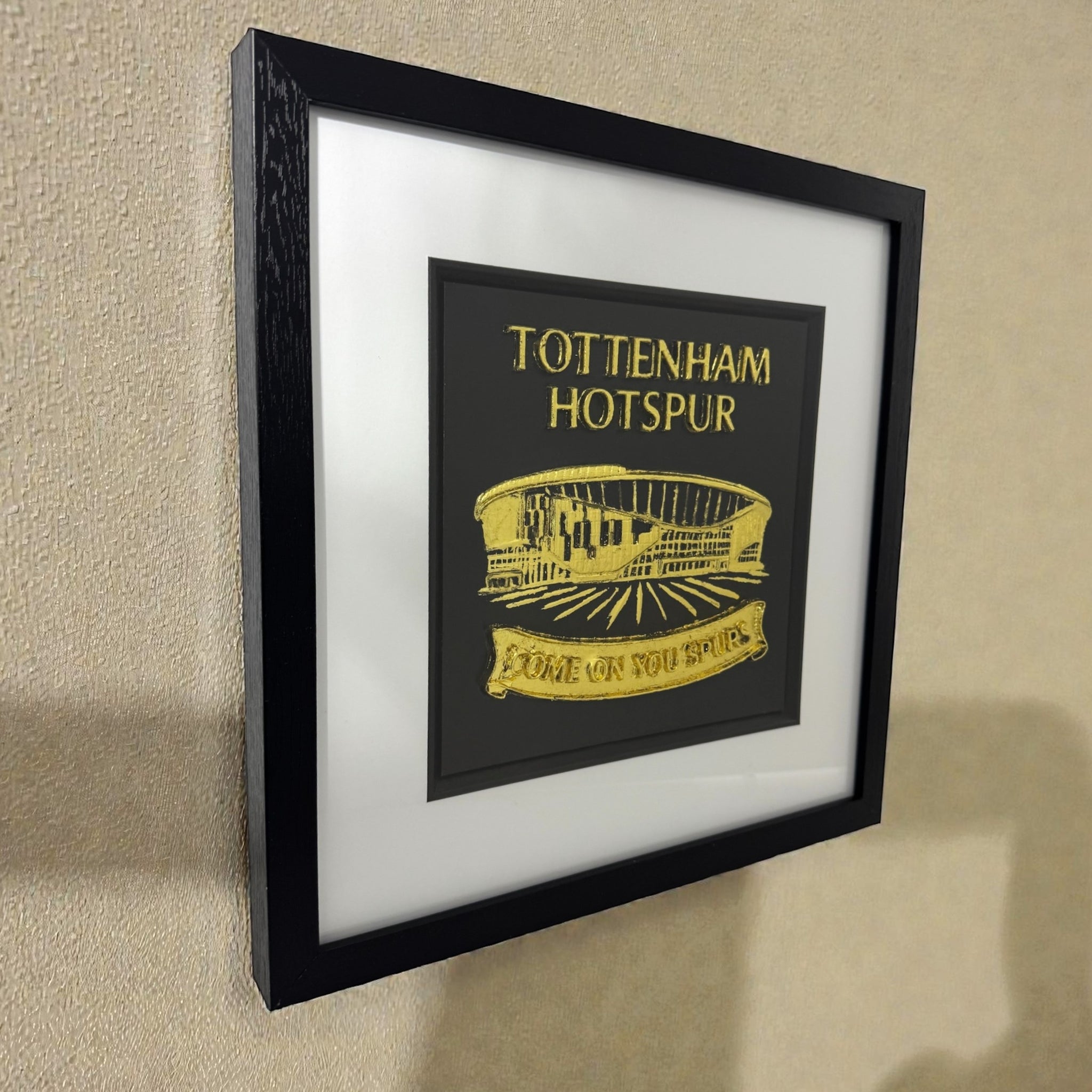 Tottenham Hotspur stadium wall art in gold leaf 3D relief, black box frame with white mount, angled wall view showing depth and shadow