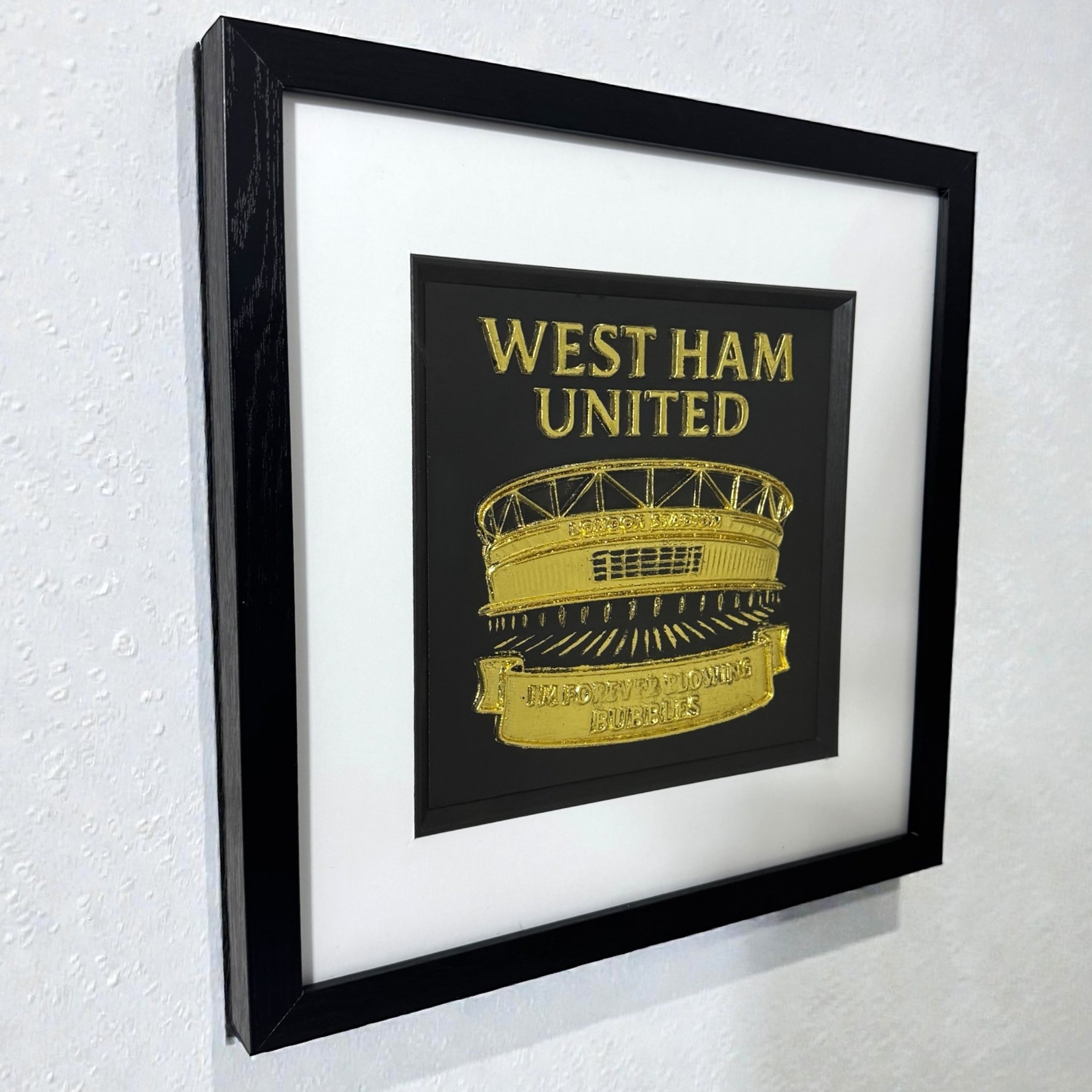 Framed West Ham United stadium wall art in gold leaf displayed on a wall with white mount and black frame