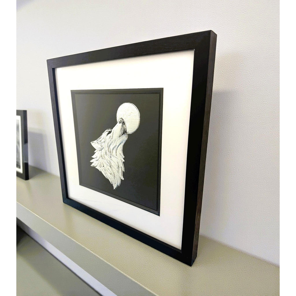 Wolf howling at the moon wall art in silver leaf, framed in black with white mount