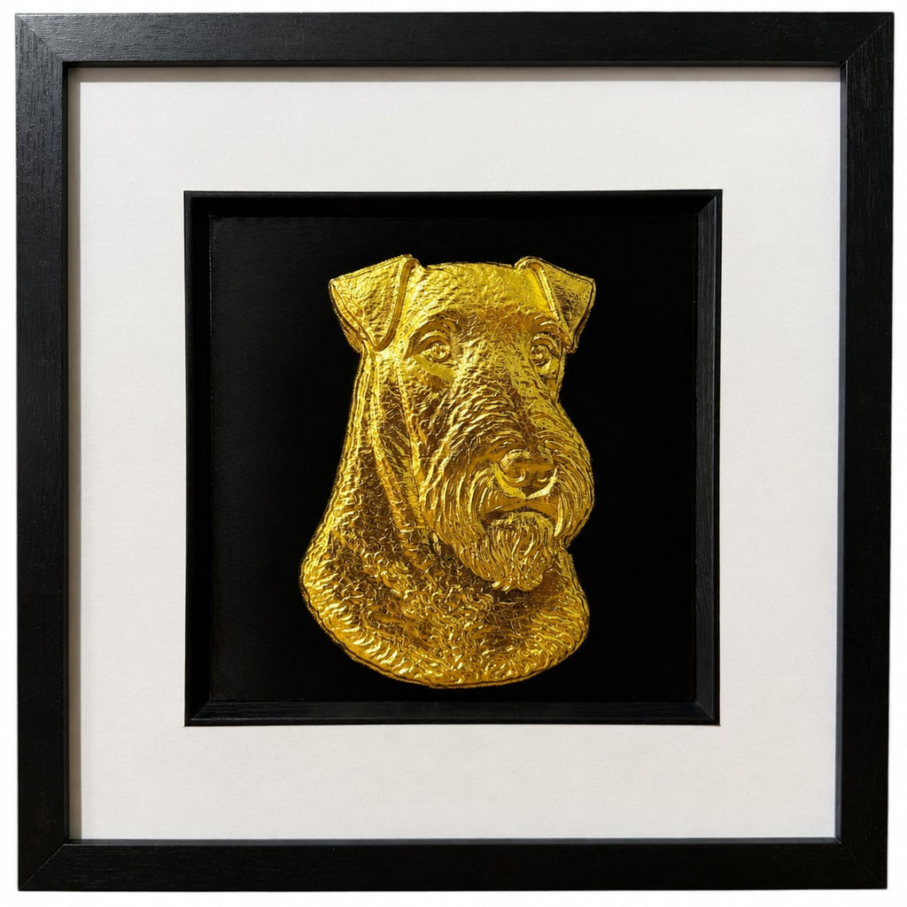 Framed Airedale Terrier wall art, gold relief portrait with folded ears and beard on a black background, black wooden frame with white mount, on a white background