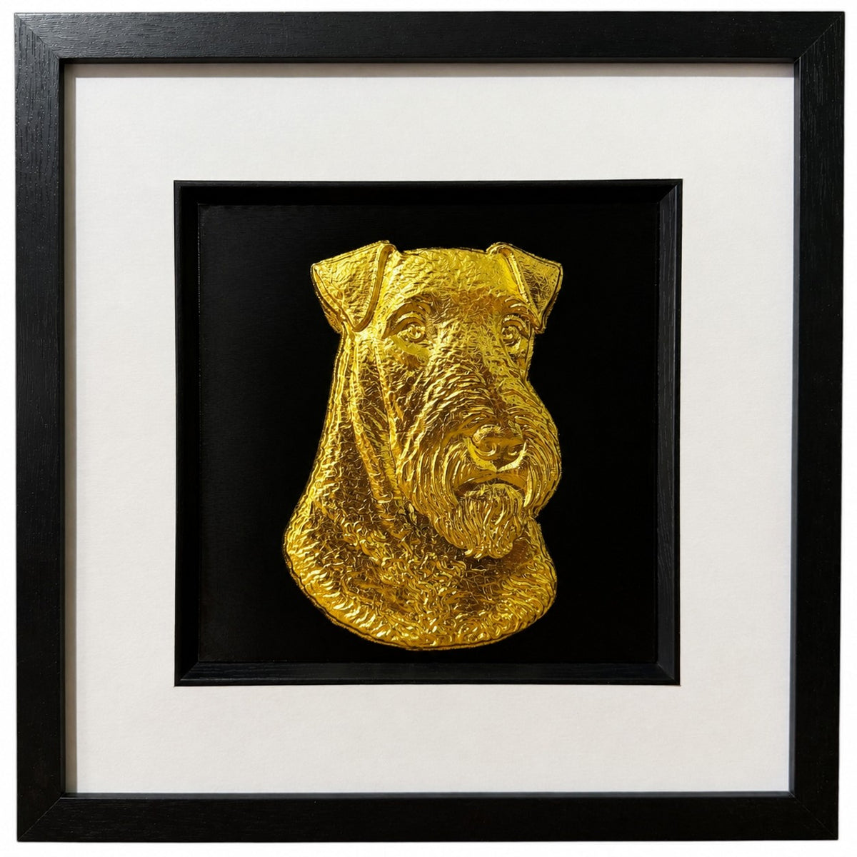 Framed Airedale Terrier wall art, gold relief portrait with folded ears and beard on a black background, black wooden frame with white mount, on a white background