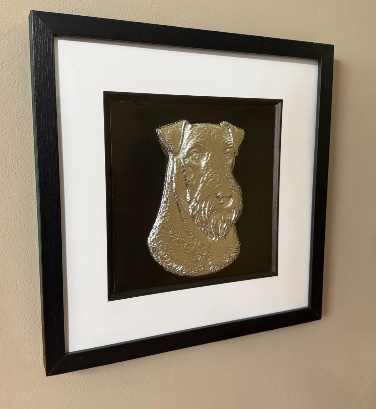 Gold Airedale Terrier 3D wall art hanging on a cream textured wall, viewed from the side to show the depth of the black box frame and the raised beard