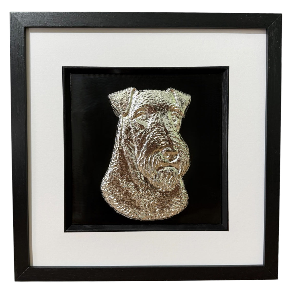 Framed Airedale Terrier wall art, silver relief portrait of the wiry head and beard on a black background, black wooden frame with white mount, on a white background