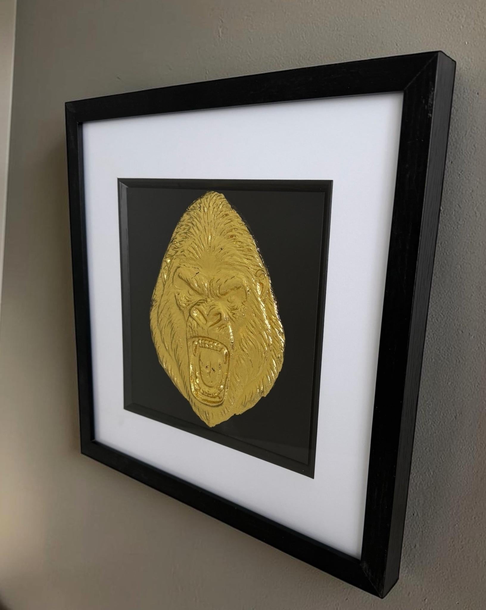 Angled lifestyle wall shot of the Gold finish gorilla piece, showing the raised relief, black box frame depth, white mount, black inner surround and neutral room styling.