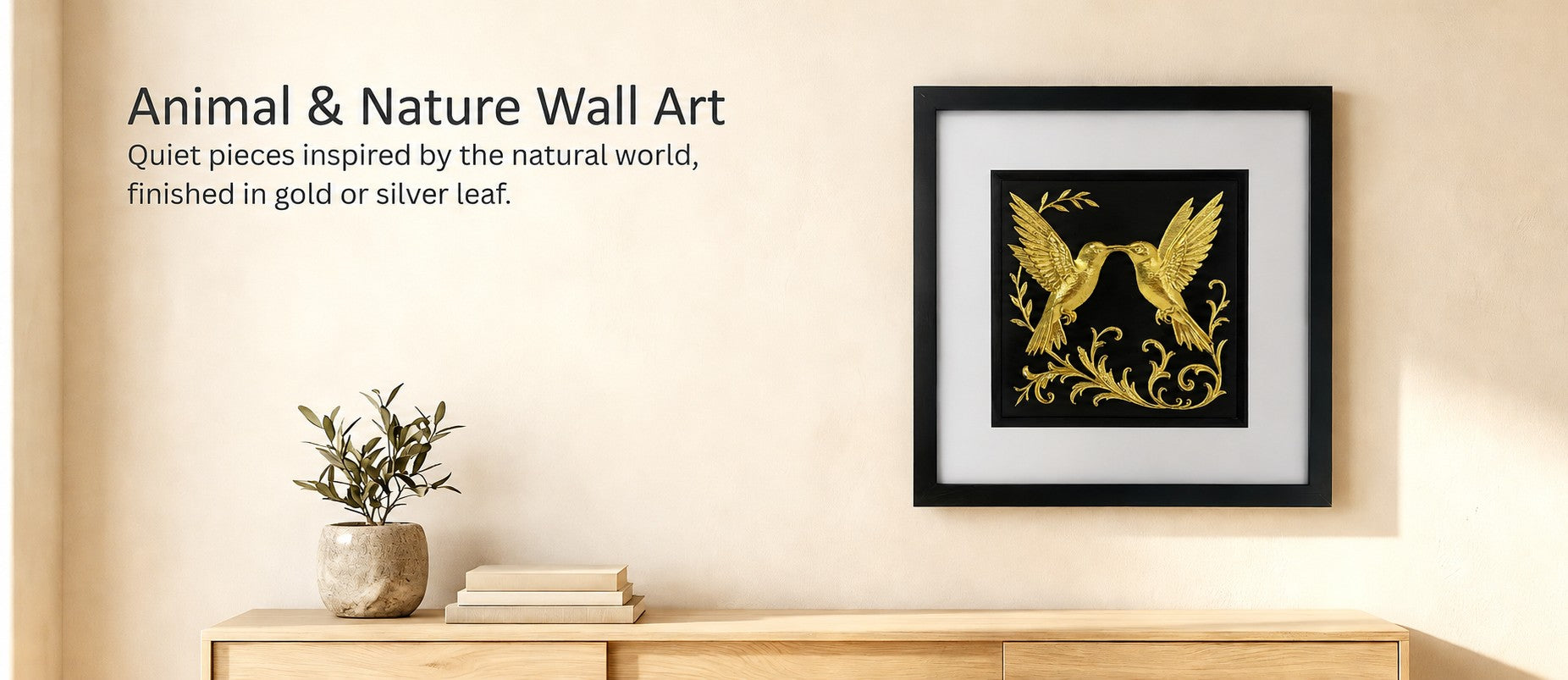 Lifestyle image showing gold hummingbird wall art in a black frame with white mount, displayed above a wooden console with Animal & Nature Wall Art text.