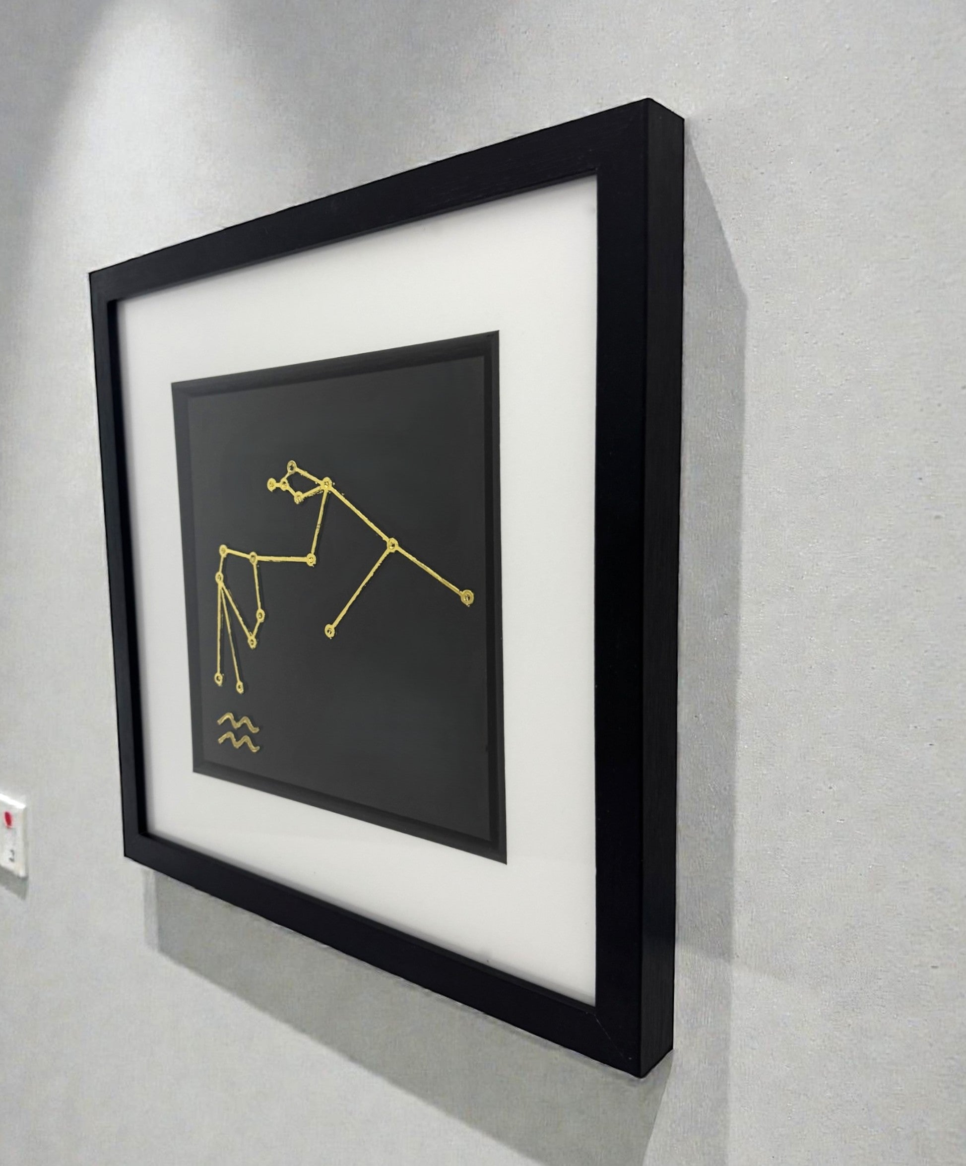 Framed gold Aquarius constellation wall art displayed on a wall, black frame with white mount and Aquarius star pattern