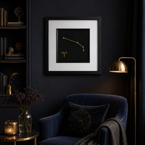 Aries zodiac constellation framed wall art in gold displayed on a dark wall with celestial decor, velvet chair, warm lighting and gold accents.