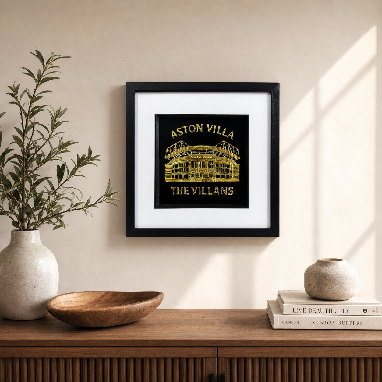 Gold Aston Villa Villa Park wall art displayed on a neutral wall above a wooden sideboard with decorative vase and bowl.