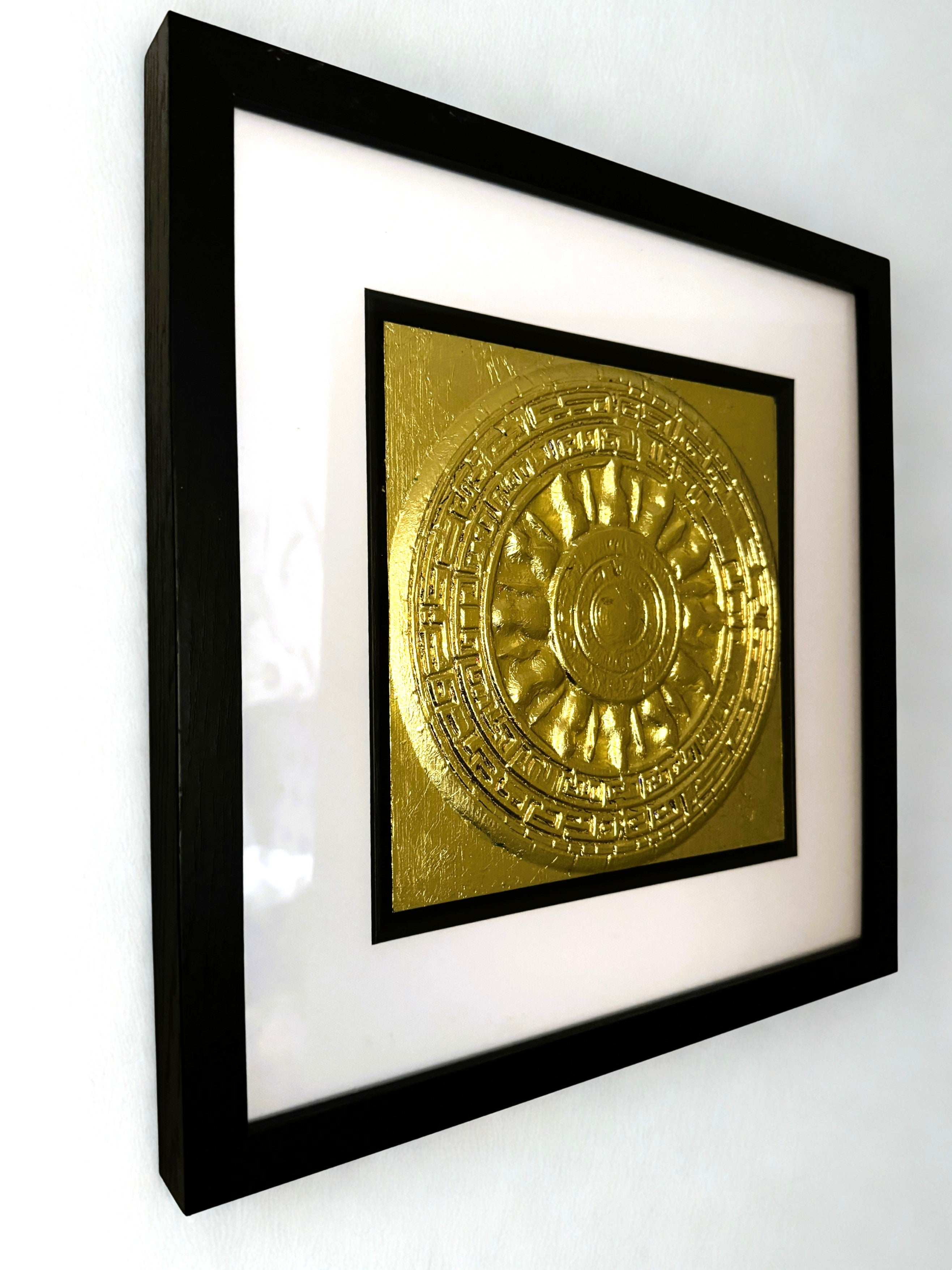 Angled wall-mounted gold leaf Aztec Sunstone wall art shown in a black frame