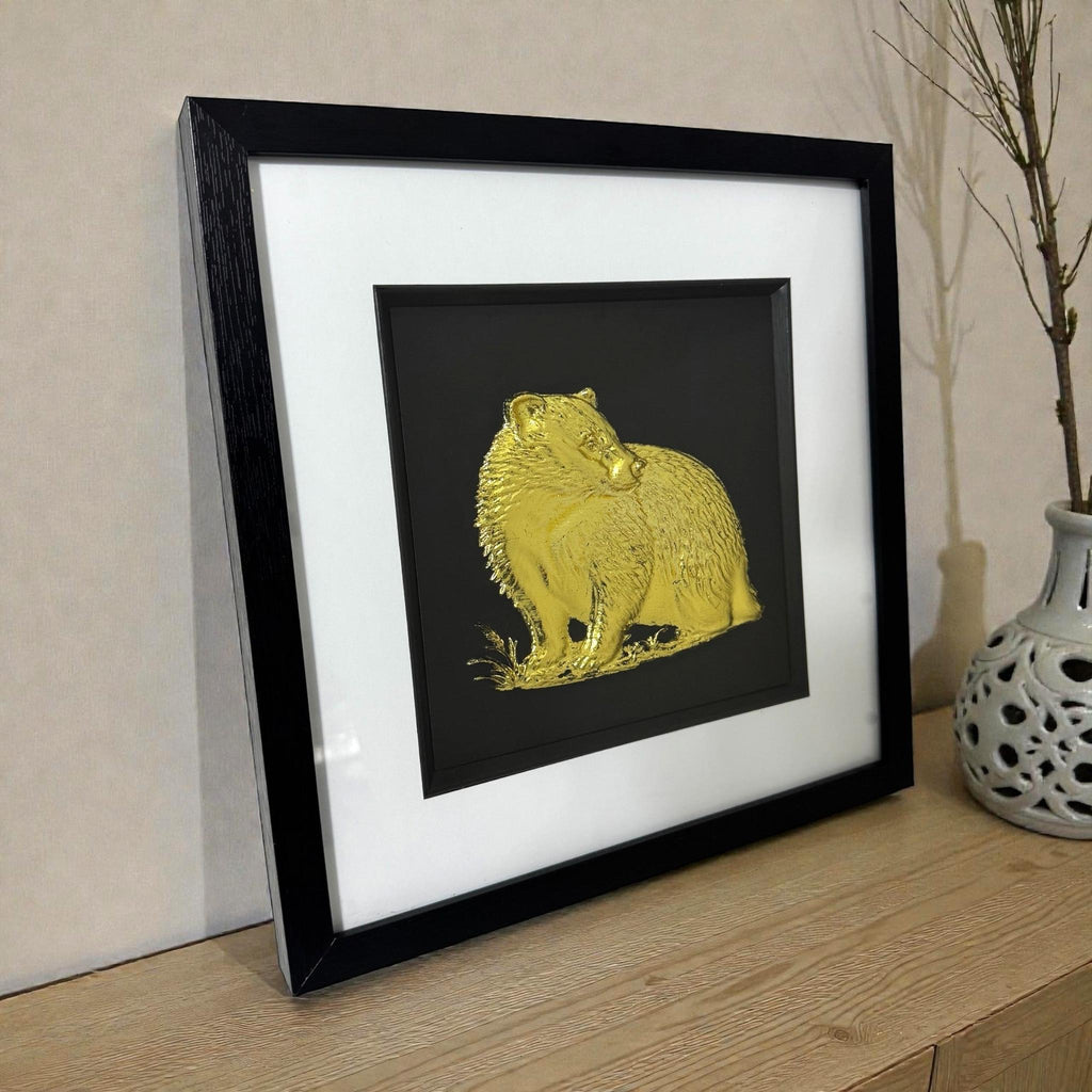 Framed badger 3D wall art in gold leaf, in a black frame with white mount, styled on a wooden surface with a vase.