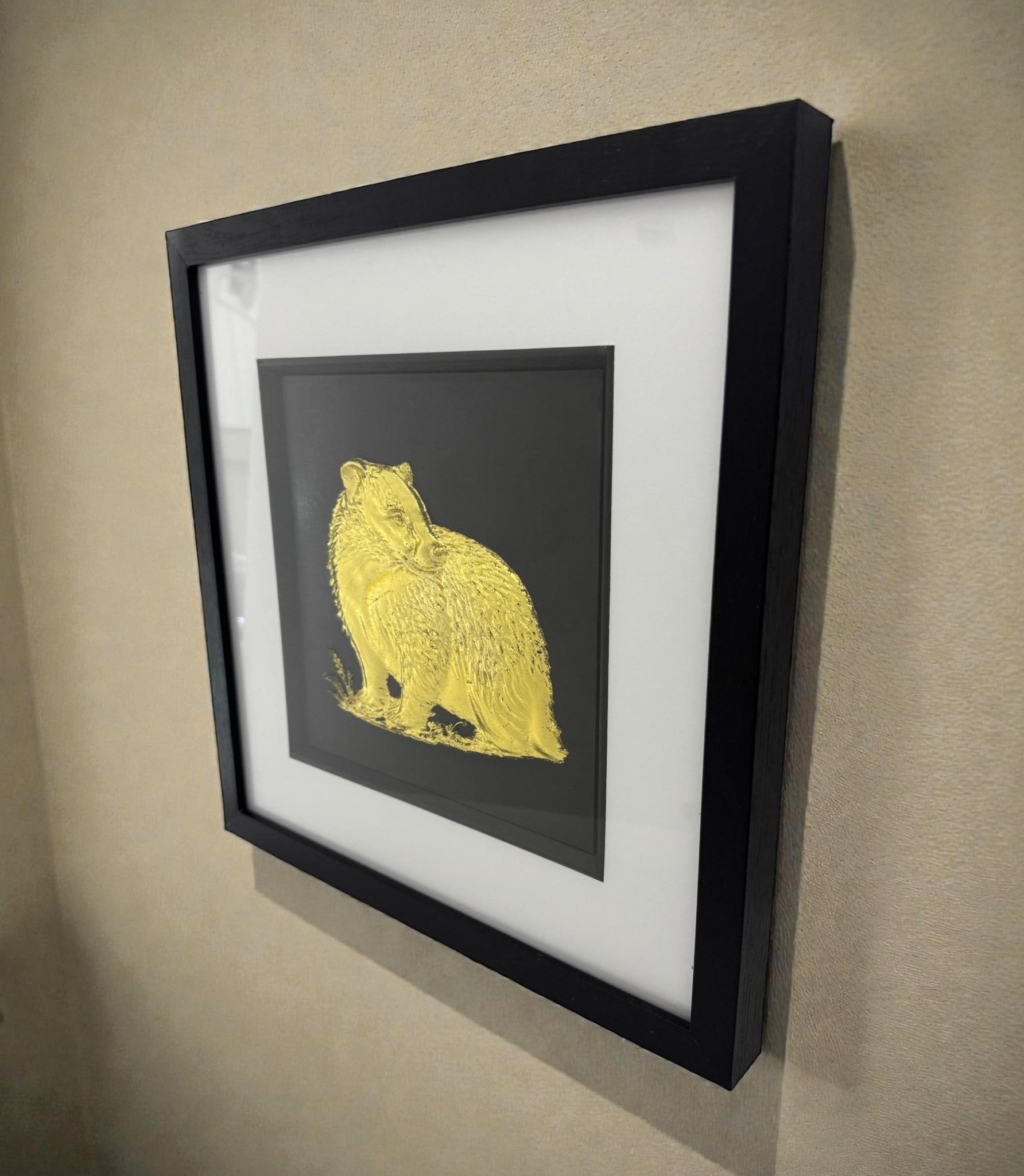 Side view of framed badger 3D wall art in gold leaf, in a black frame with white mount, hung on a beige wall.