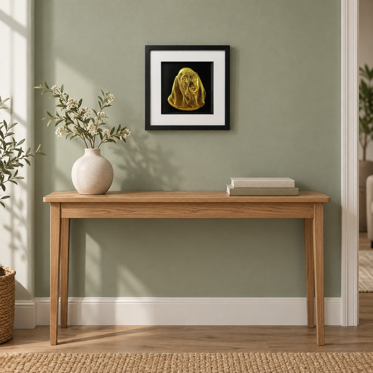 Gold Basset Hound 3D wall art in a black square frame hung on a sage green wall above an oak console table with a vase of white blossom and two linen books