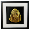 Framed Basset Hound wall art, gold relief portrait of the head and long ears on a black background, black wooden frame with white mount, on a white background