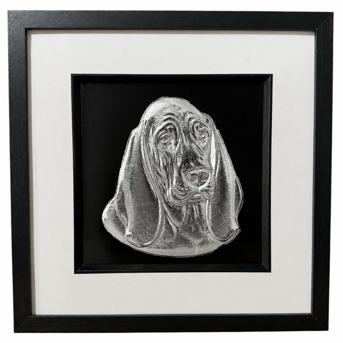 Framed Basset Hound wall art, silver relief portrait of the head and drooping ears on a black background, black wooden frame with white mount, on a white background