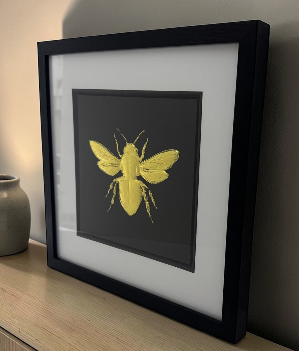 Angled view of gold leaf bumble bee framed artwork displayed on a shelf