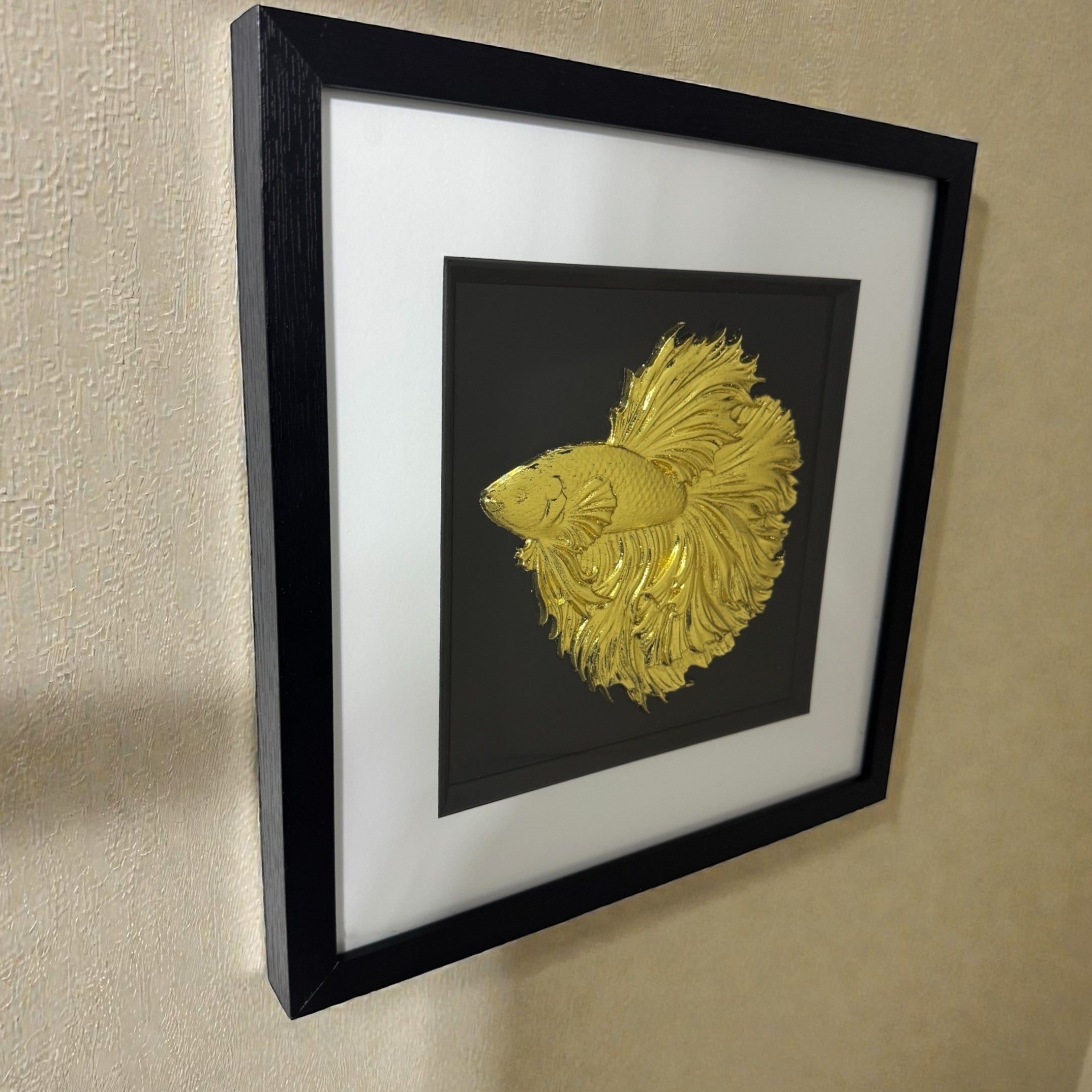 Side angle view of the Betta Fish wall art hanging on a wall, highlighting the raised relief sculpture and how the metallic gold catches the light.