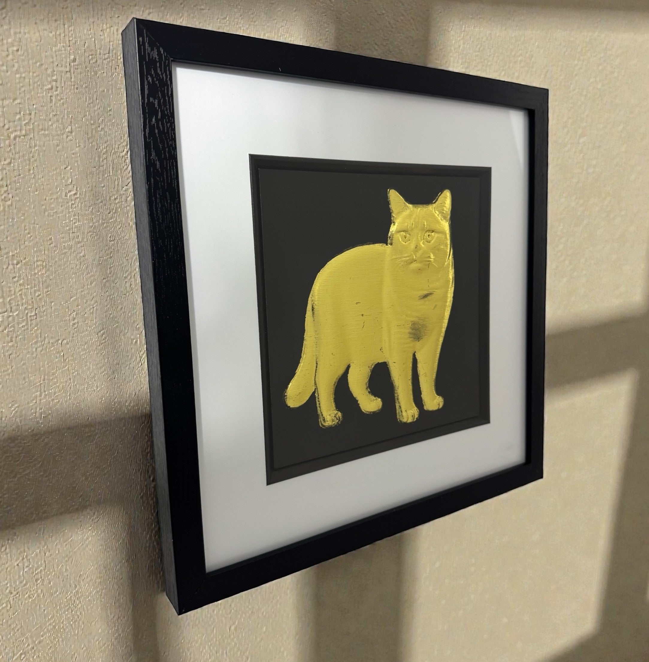 Lifestyle photo of framed British Shorthair cat wall art in gold leaf 3D relief hanging on wall, black frame white mount, soft natural light