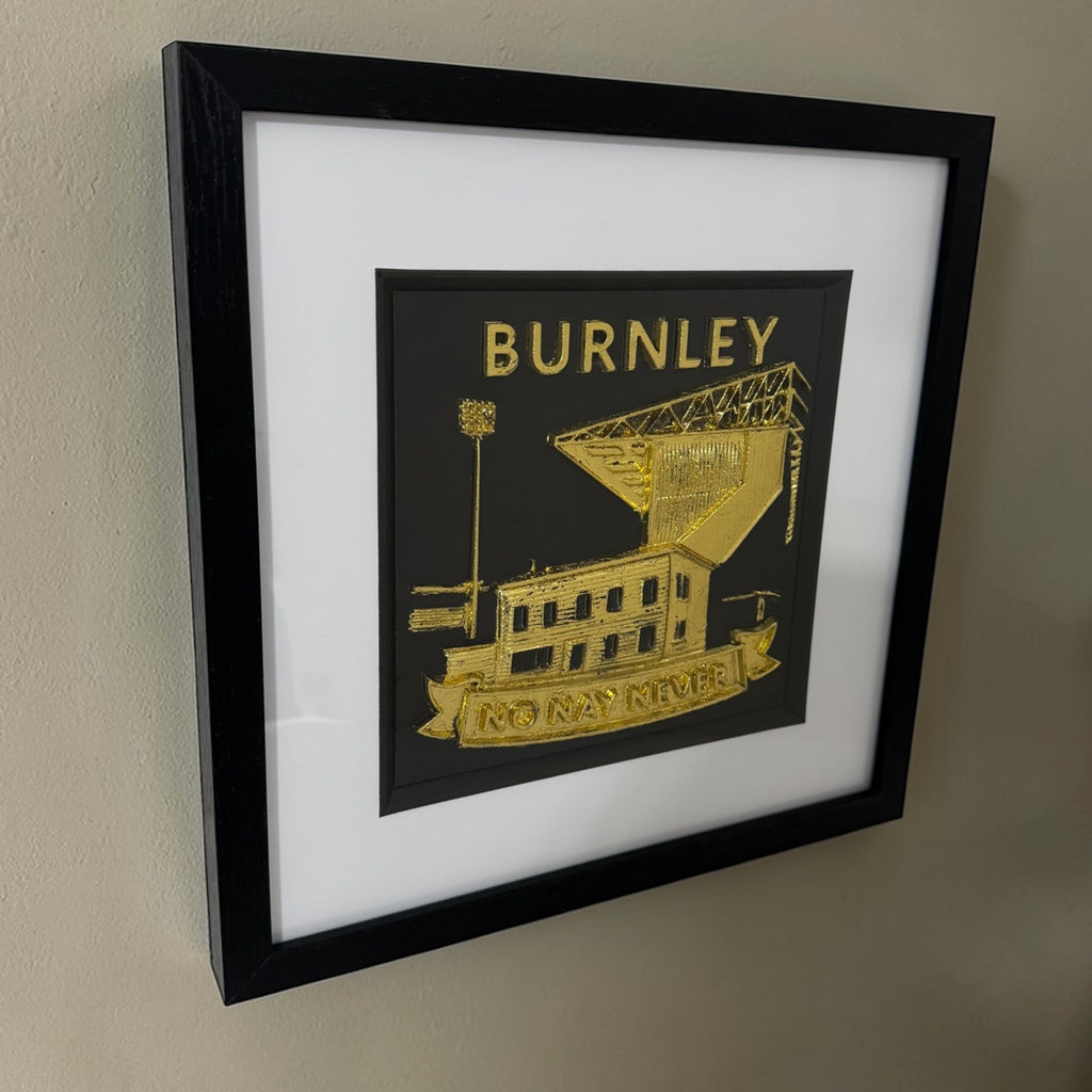 Side view of a gold Burnley football club framed relief hanging on a neutral wall.