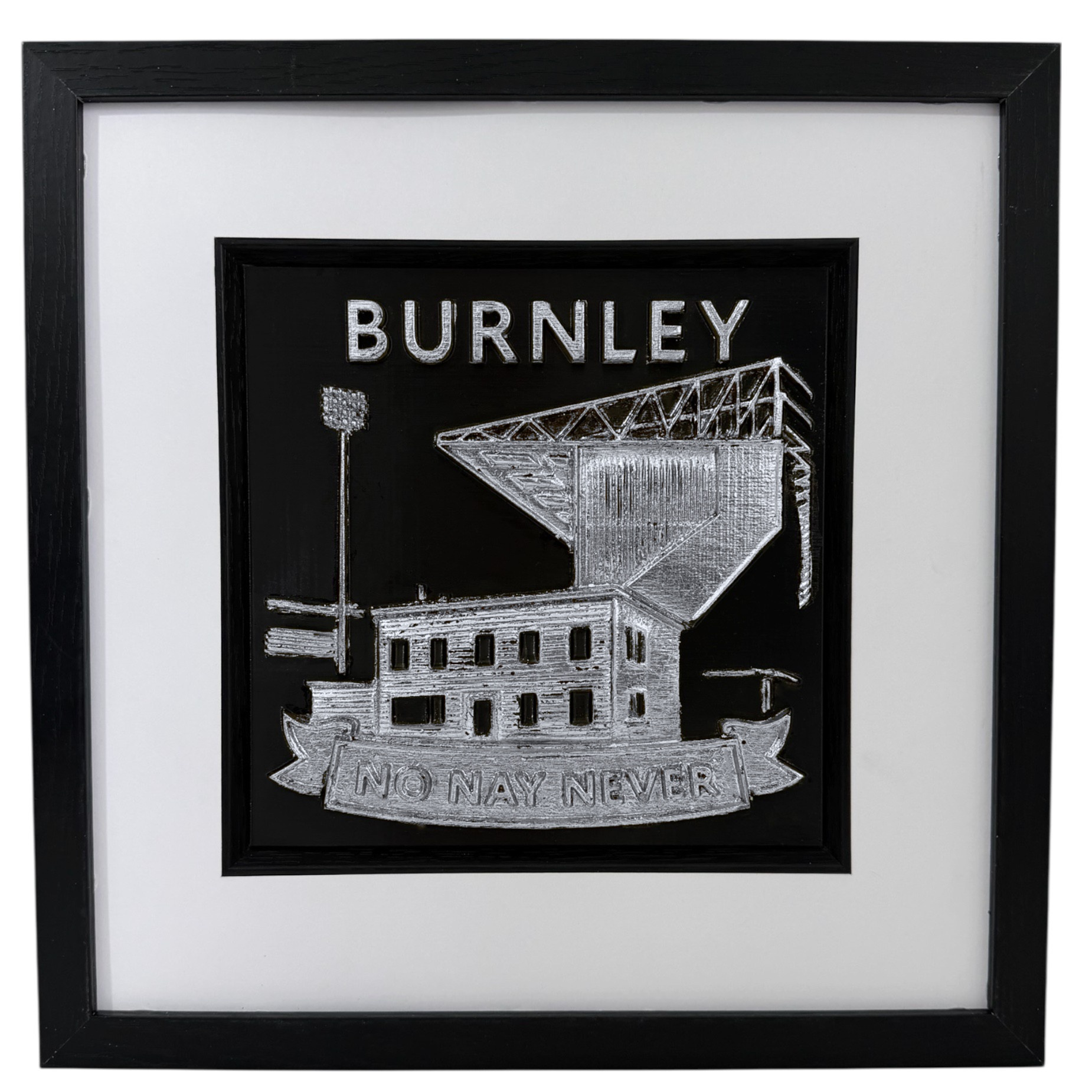 Front view of a silver Burnley football club relief in a black frame with wide white mount and black inner surround.