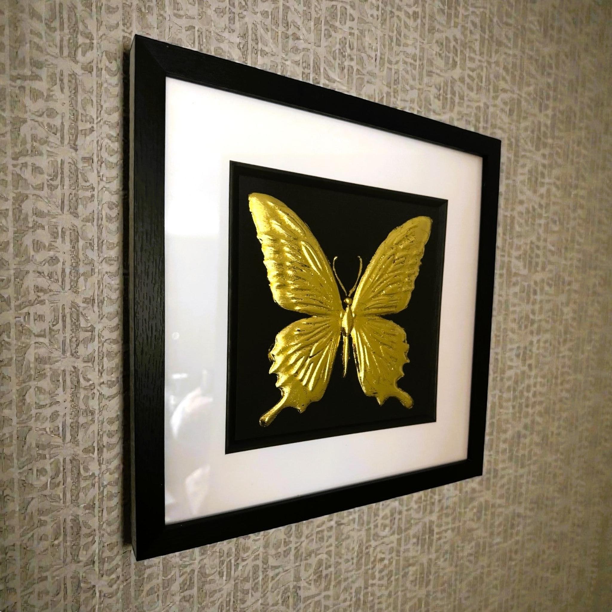 Gold butterfly wall art framed in black with white mount on a textured wall