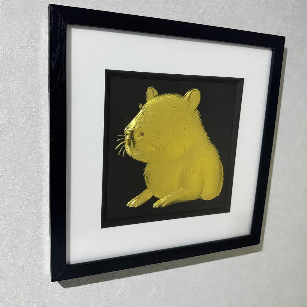 Capybara portrait wall art in gold leaf shown hanging on a light textured wall in a black frame with white mount