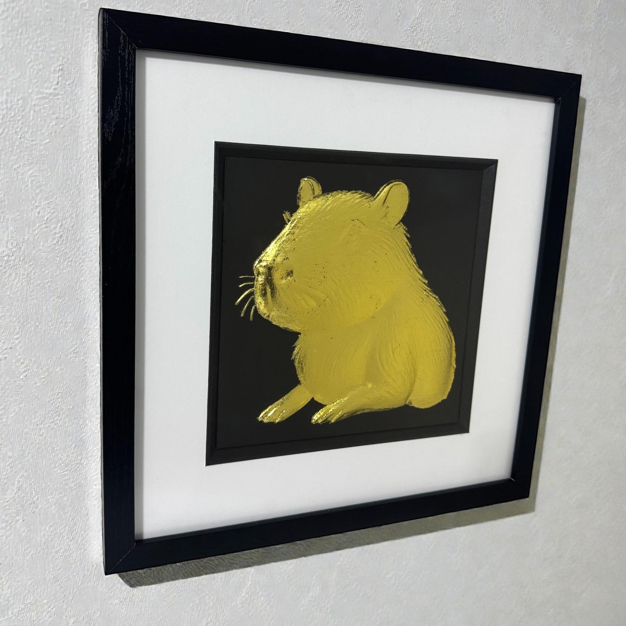 Capybara portrait wall art in gold leaf shown hanging on a light textured wall in a black frame with white mount