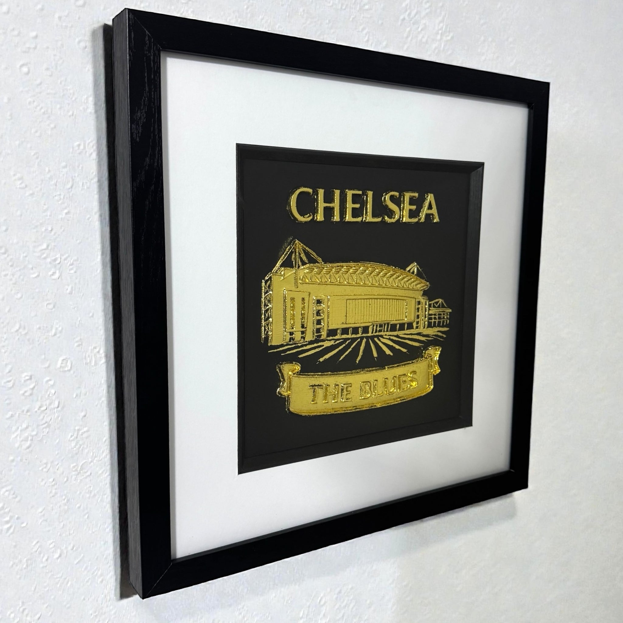 Framed Chelsea stadium wall art in gold leaf displayed on a wall with white mount and black frame
