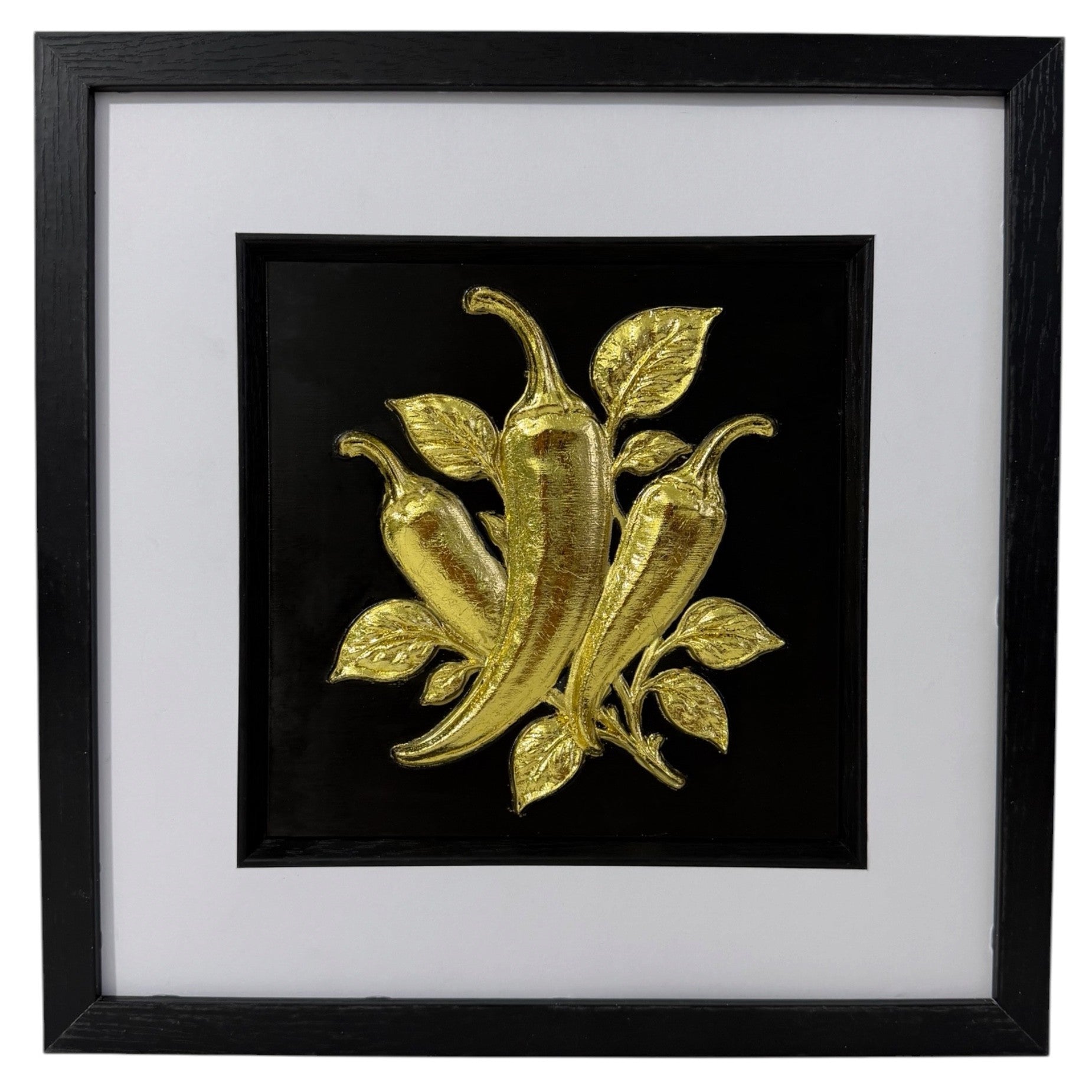Gold chilli pepper raised relief artwork in a black frame with leafy detail and white mount.