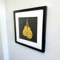Side view of framed boxing gloves 3D wall art in gold leaf, in a black frame with white mount, hung on a white wall.