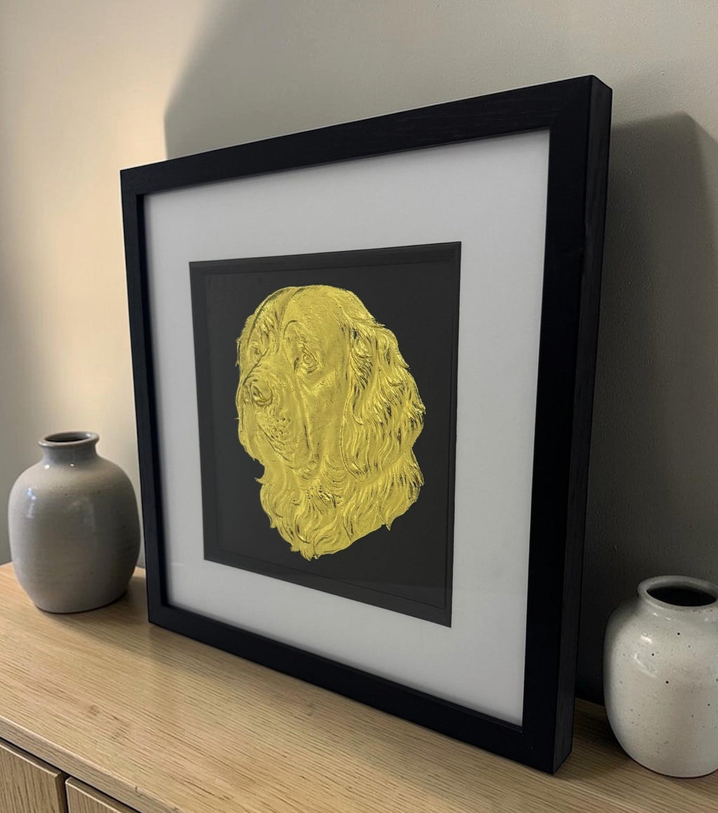 Gold Clumber Spaniel wall decor styled in a black box frame on a wooden sideboard between two ceramic vases.