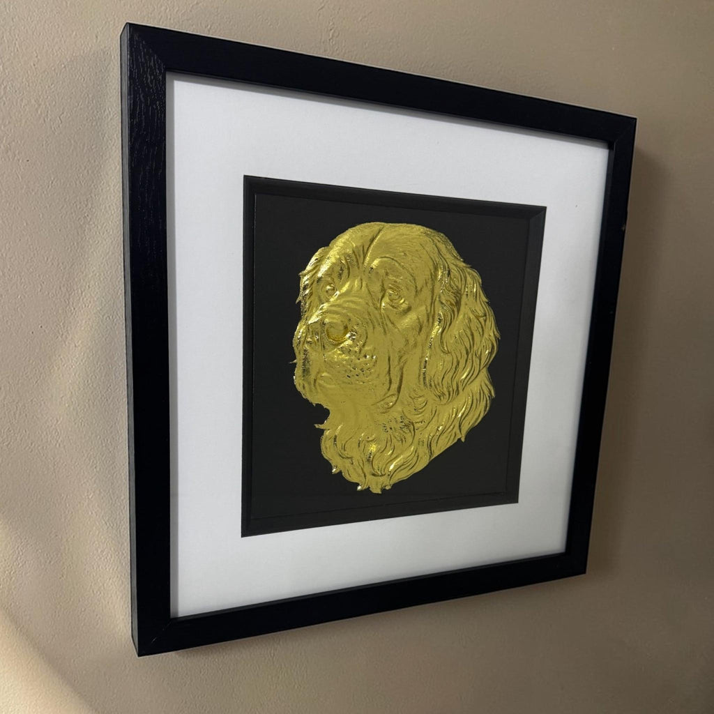 Angled view of a gold Clumber Spaniel relief in a black box frame with glass front hanging on a neutral wall.