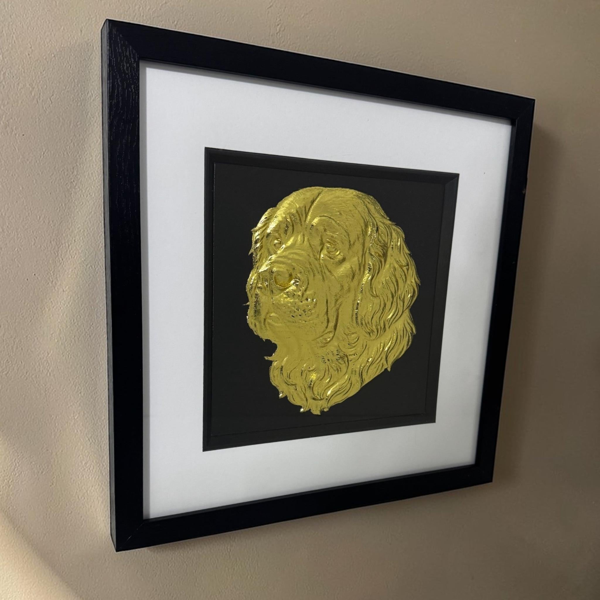 Angled view of a gold Clumber Spaniel relief in a black box frame with glass front hanging on a neutral wall.