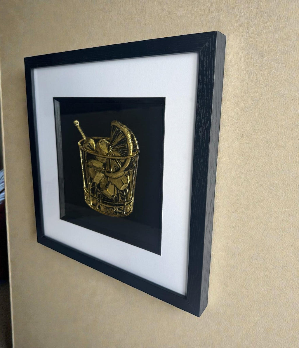 Angled wall view of framed cocktail glass Gold Leaf relief artwork, black box frame with white mount and inner black surround