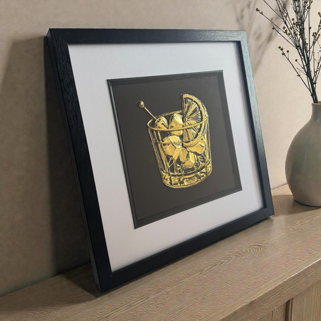 Framed cocktail glass Gold Leaf relief artwork styled on a wooden sideboard, black box frame with crisp white mount and inner black surround