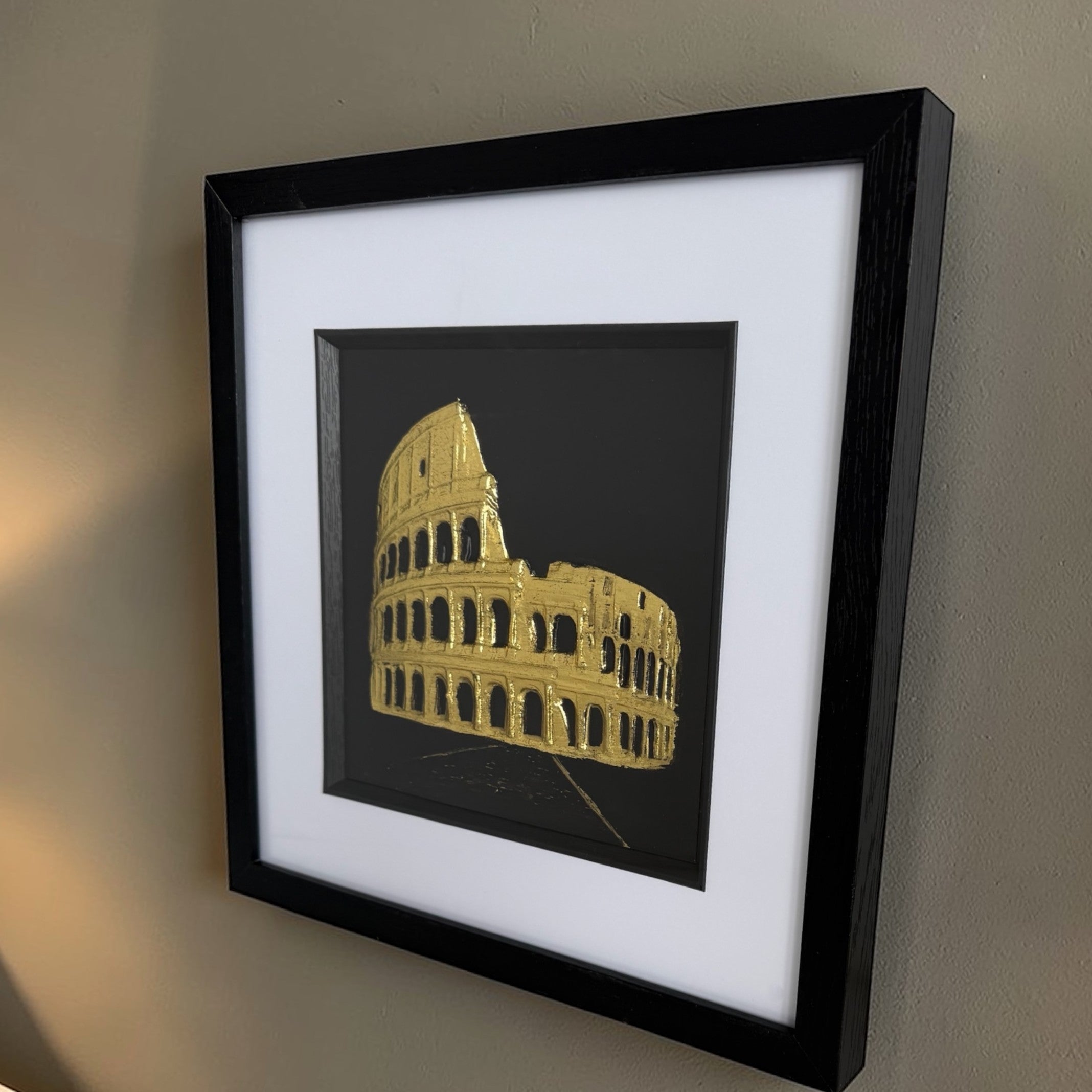 Gold Colosseum raised relief styled as wall decor on a neutral interior wall with warm lamp light.