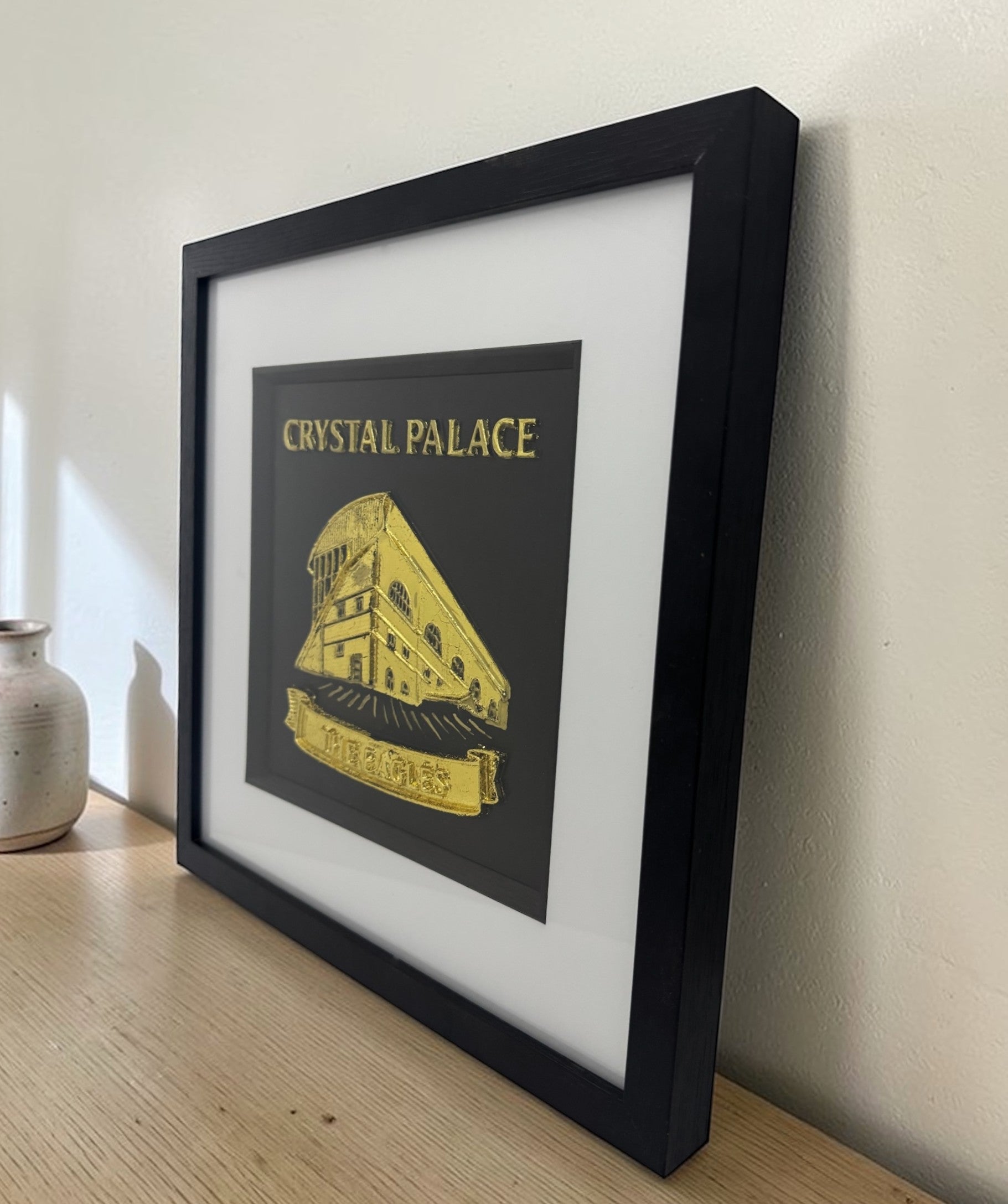 Gold Crystal Palace stadium 3D relief framed artwork on shelf, angled side view showing frame depth and glass reflections