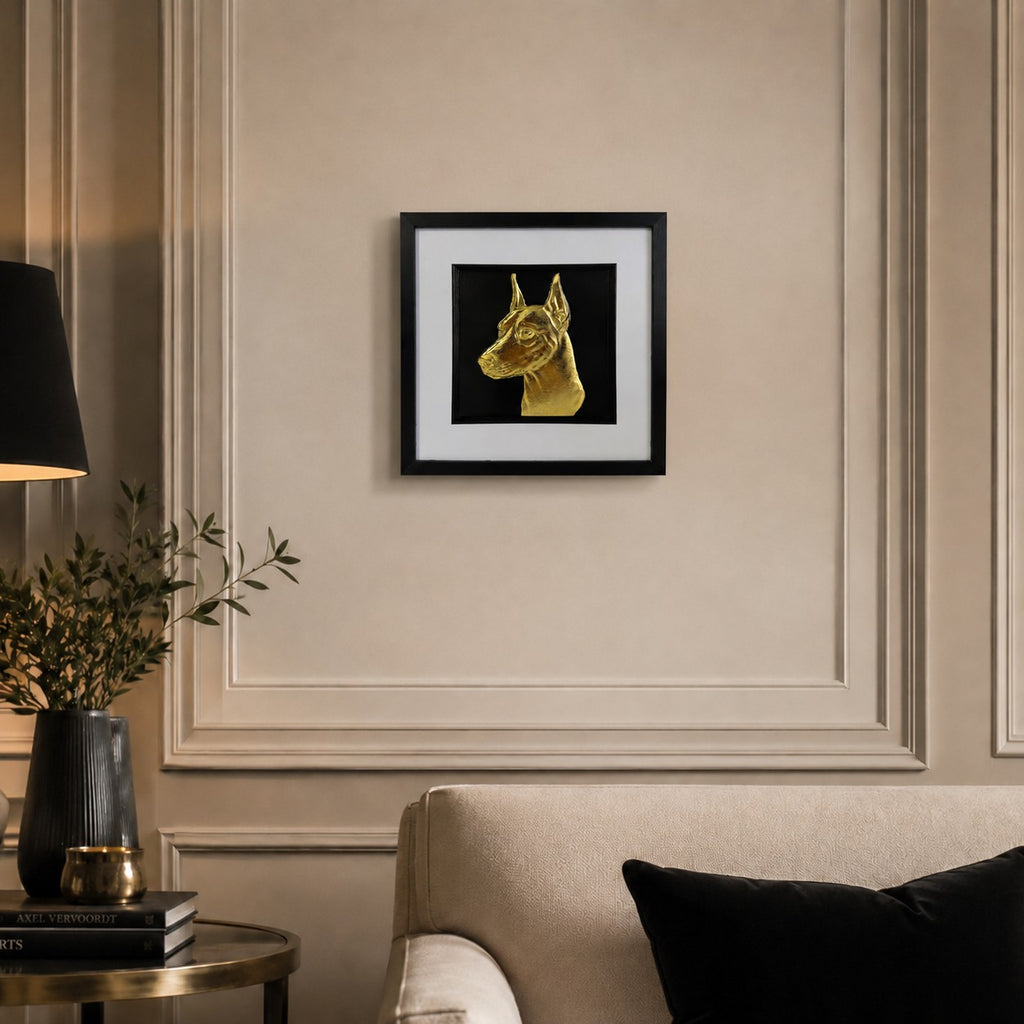 Doberman gold leaf framed dog wall art displayed above a cream sofa in a warm neutral living room with black and gold accents.