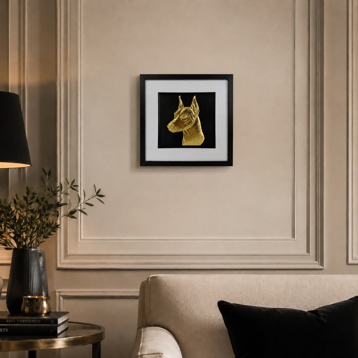 Doberman gold leaf framed dog wall art displayed above a cream sofa in a warm neutral living room with black and gold accents.
