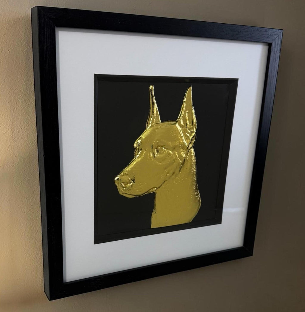 Framed gold doberman relief portrait with glass front hanging on a neutral wall.