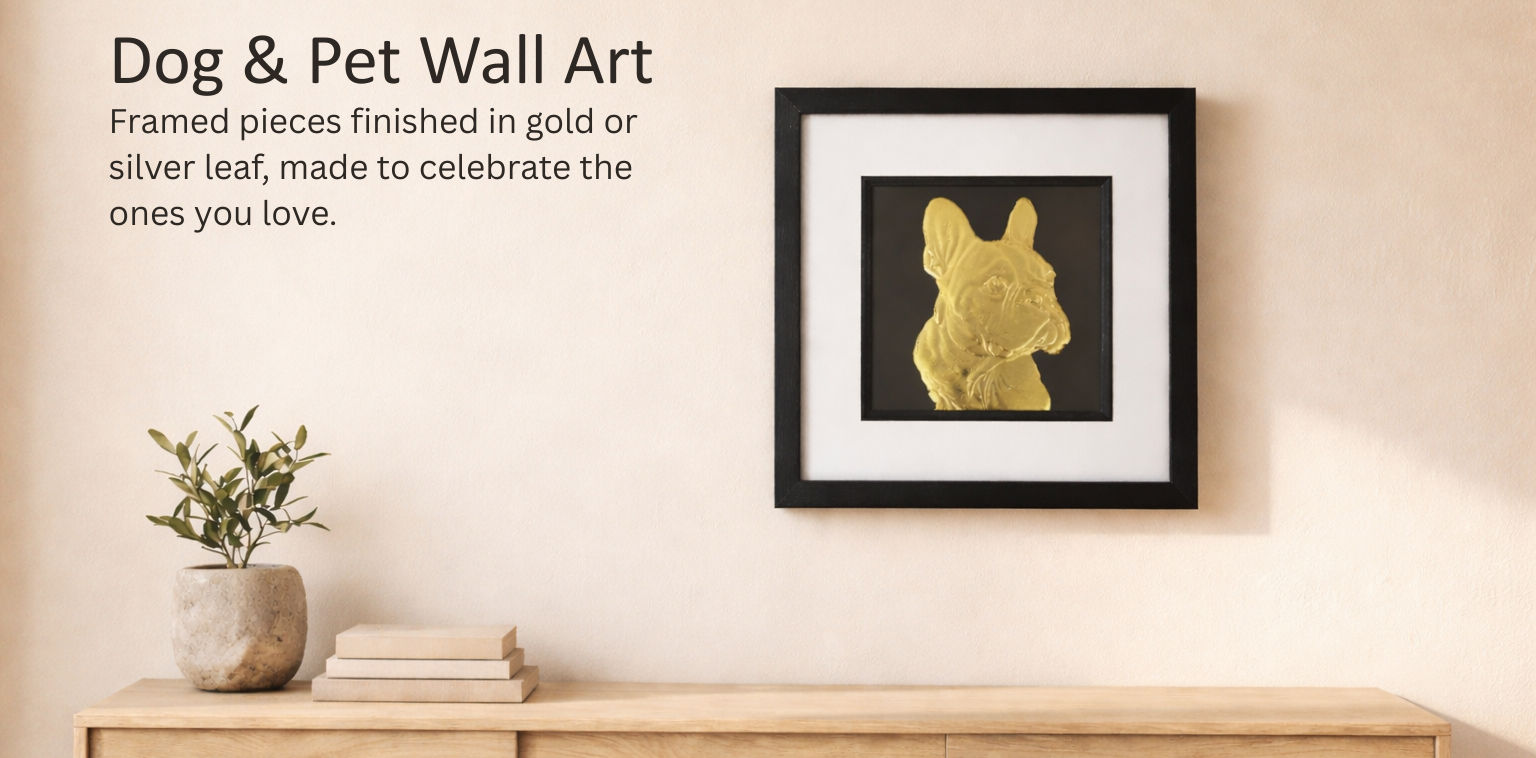 Hero banner for JP Designs Dog & Pet collection showing a framed gold leaf French bulldog wall art on a warm off-white plaster wall above a light oak console, with a small plant and neutral books on the left and soft daylight from the left.
