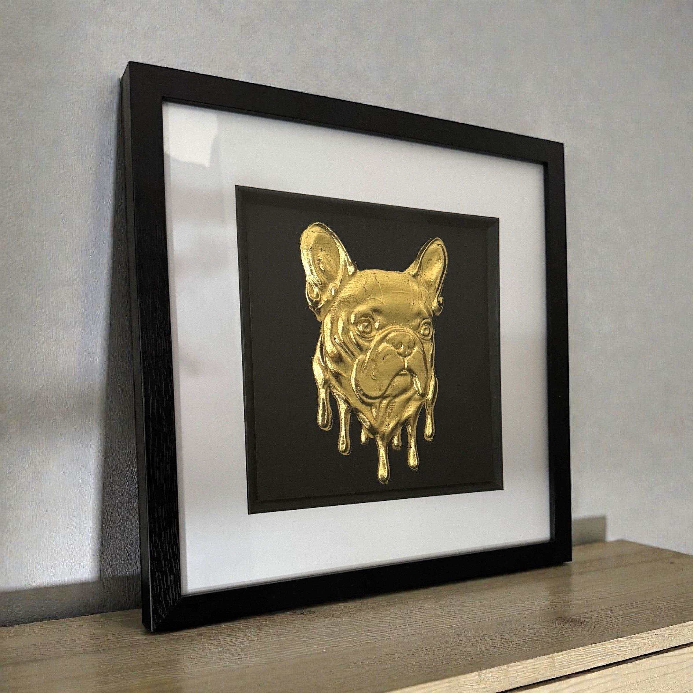 Molten French Bulldog gold leaf wall art in black frame and white mount photographed on a desk at a slight angle