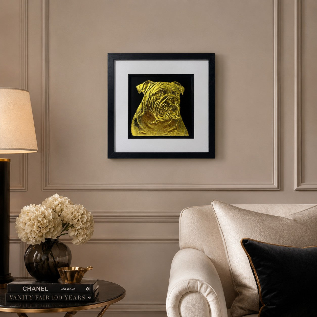 English Bulldog gold leaf framed dog wall art displayed above a cream sofa in a warm neutral living room with black and gold accents.