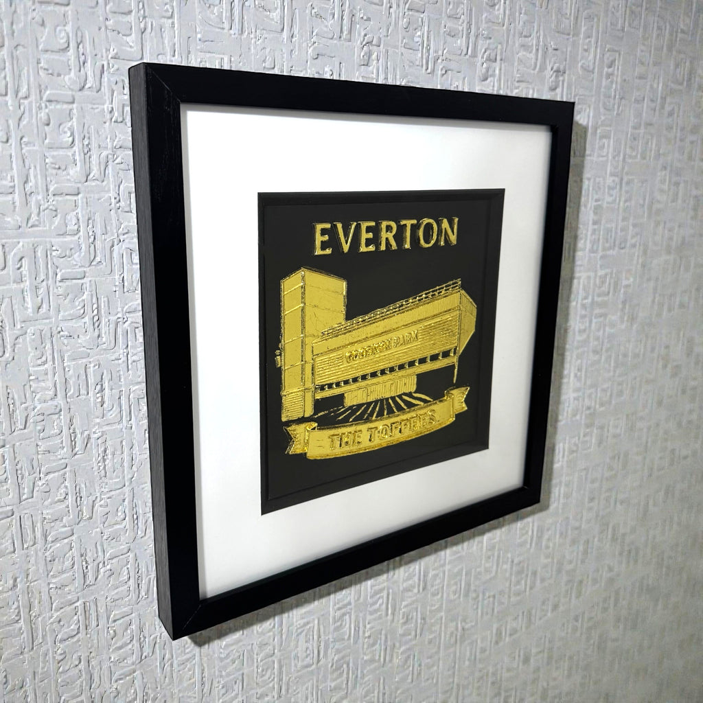 Framed Everton stadium wall art in gold leaf displayed on a wall with white mount and black frame