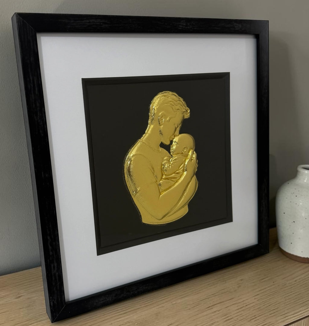 Gold father and baby framed 3D artwork styled on a sideboard with neutral ceramic vase.