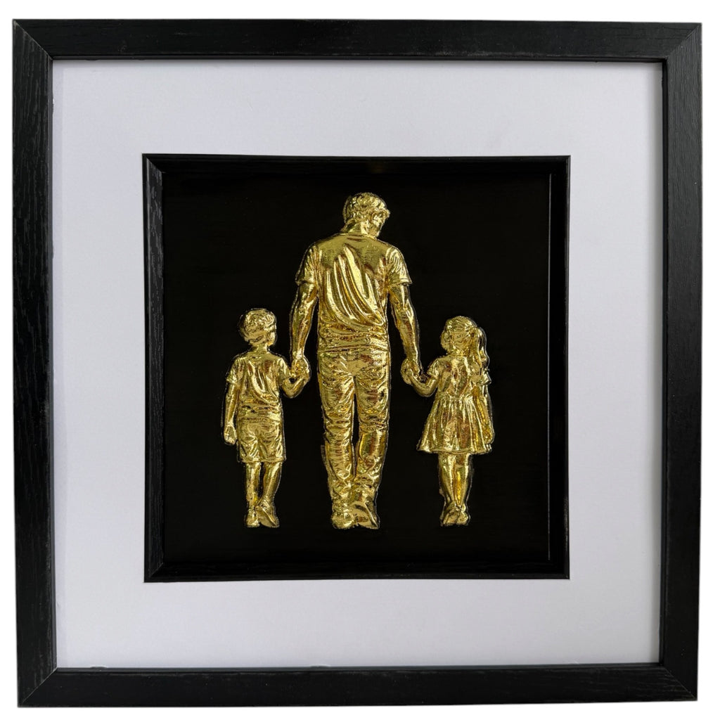 Gold father holding hands with son and daughter relief artwork in a black frame with white mount.
