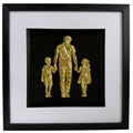 Gold father holding hands with son and daughter relief artwork in a black frame with white mount.