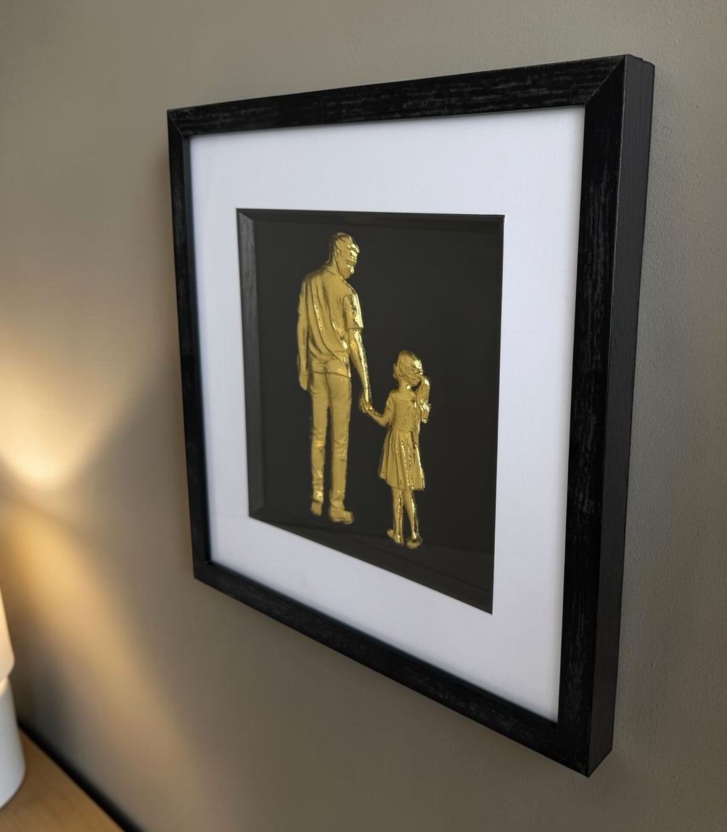 Gold father and daughter framed wall art mounted on a warm neutral wall, showing a sentimental parent and child design in a black frame with white mount.