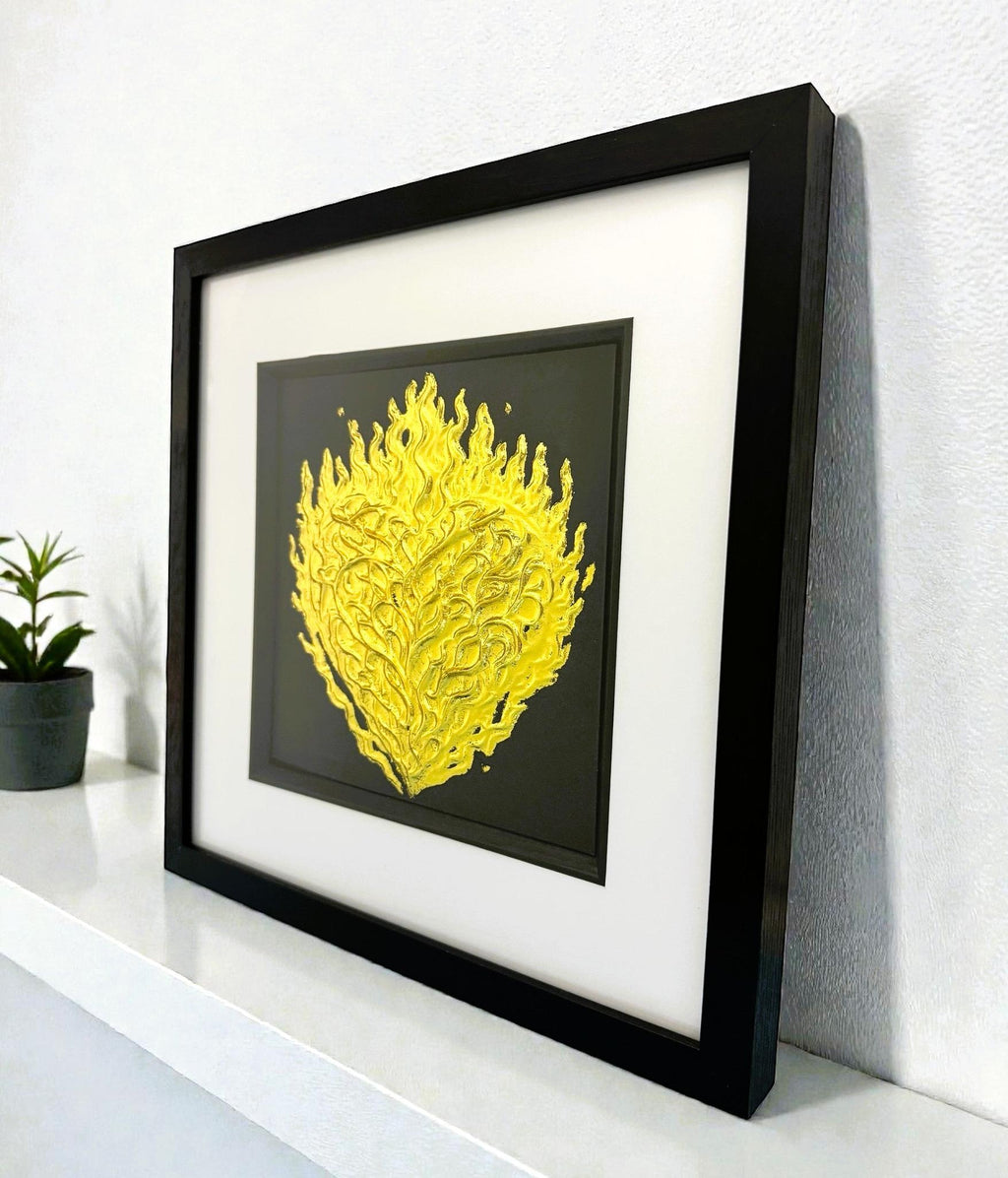 Angled desk view of gold leaf flaming heart wall art on a black background in a black wooden frame
